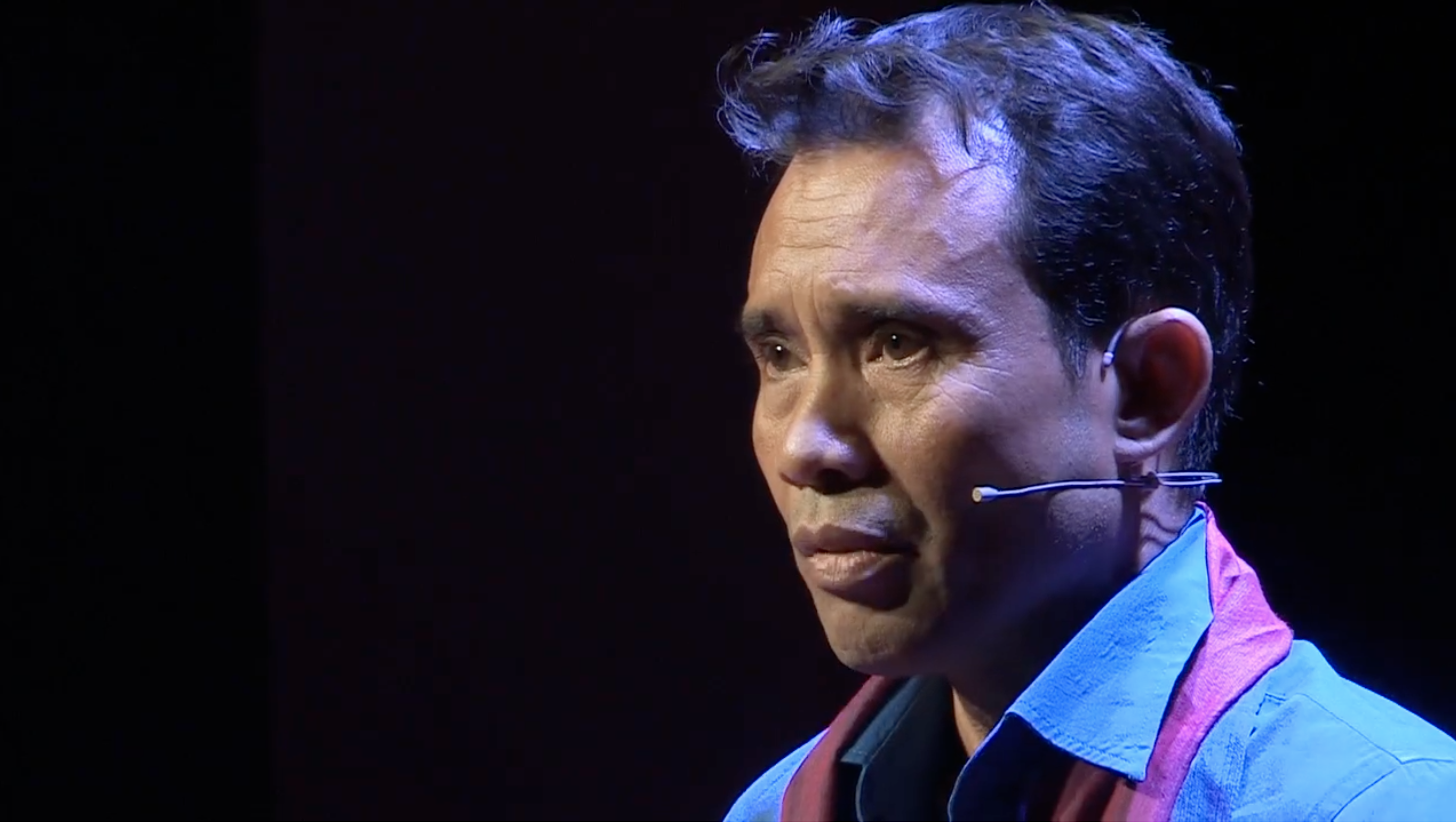 Arn Chorn-Pond speaking at TEDx, illuminated by stage lighting